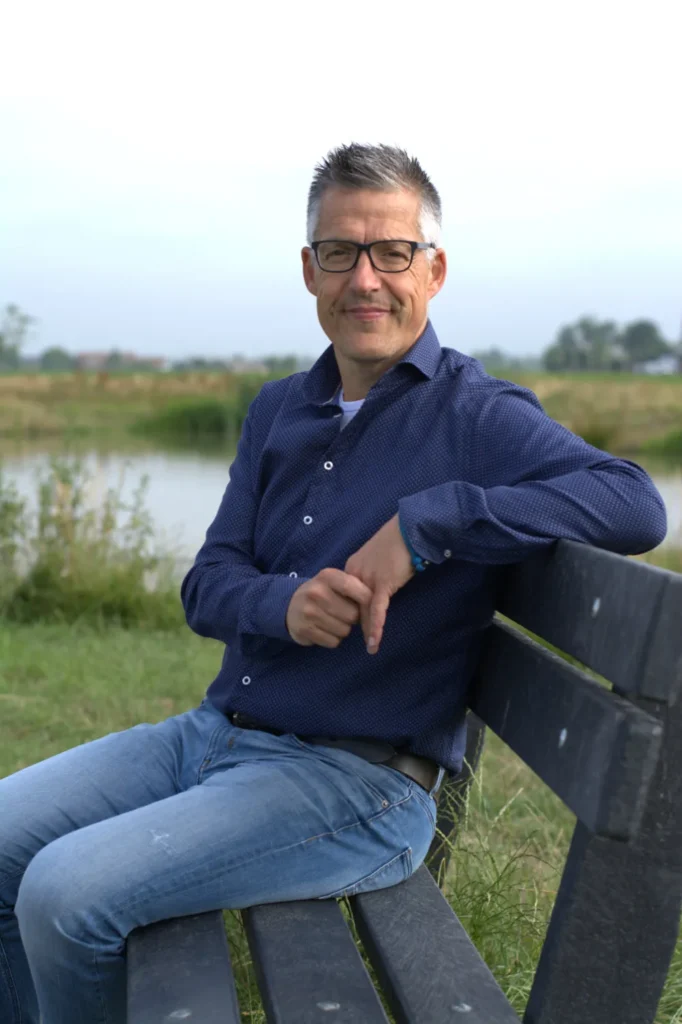 Man zit op bankje bij water in natuur